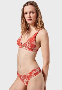 Conjunto de bikini rojo que presenta un top triangular modificado con un patrón floral y unas braguitas de tiro bajo a juego, fabricado con una suave tela elástica.