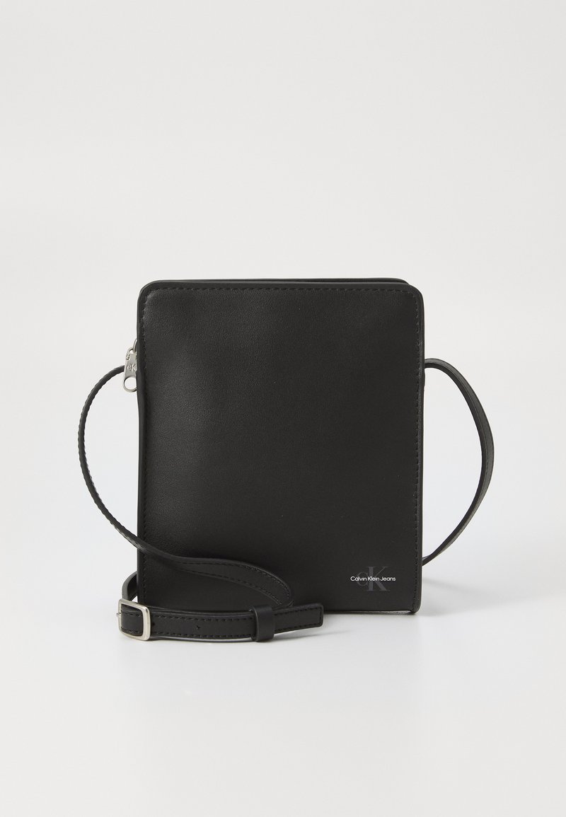 Melna ādas crossbody soma ar kvadrāta formu, rāvējslēdzēja aizdare un šaura regulējama siksna. Priekšpusē ir Calvin Klein Jeans logotips.