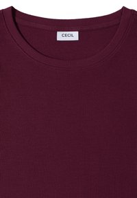 Haut bordeaux côtelé à manches courtes avec un col rond et une étiquette blanche indiquant "CECIL" à l’intérieur du col.