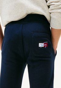 Marineblå sweatpants med en baglomme og et flerfarvet logo-patch. Stoffet ser blødt ud med en let struktur og har en elastisk talje.