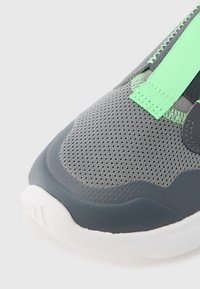 Γκρι αθλη�τικό παπούτσι με επάνω μέρος από διαπνέον πλέγμα, πράσινες λεπτομέρειες και λευκή καουτσούκ σόλα με υφή.