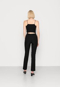 Top preto sem mangas com um design recortado na cintura, combinado com calças pretas ajustadas. O material parece suave; a silhueta é esbelta.