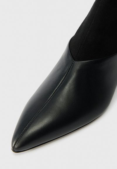 Čierne kožené čižmy s špicatou špičkou a textúrovaným čiernym semišovým zvrškom, ktoré sa vyznačujú elegantným, hladkým povrchom a štíhlym siluetou.