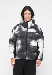 Jachetă puffer cu un model abstract alb-negru, guler înalt, fermoar pe toată lungimea și un design matlasat; are o finisaj moale și texturat.