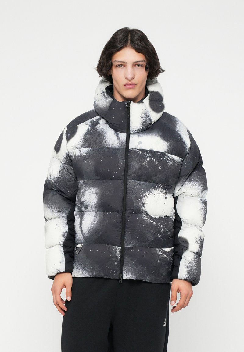 Jachetă puffer cu un model abstract alb-negru, guler înalt, fermoar pe toată lungimea și un design matlasat; are o finisaj moale și texturat.