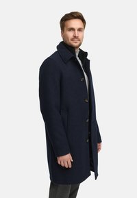 Marineblauer Wollmantel mit kragenförmigem Ausschnitt, vorderen Knöpfen und seitlichen Taschen. Das Design ist schlank und hat eine glatte Textur.