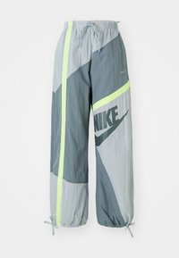 Nike träningsbyxor i grå nyanser med neon gula vertikala ränder, elastisk midja och muddar, samt en stor Nike-logotyp på det högra benet.