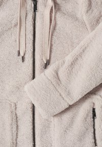 Veste en polaire rose flou avec une fermeture éclair sur toute la longueur, deux poches avant et des cordons de serrage avec le texte "Tracez votre propre chemin".