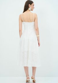 Witte bloemenkant jurk met spaghettibandjes, nauwsluitend lijfje en midi-lengte rok. Heeft een verborgen rits aan de achterkant en delicate borduursels.