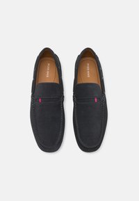 Mocassins en daim bleu marine avec une texture lisse, présentant un petit accent rouge et bleu, des coutures délicates et un design classique à enfiler.