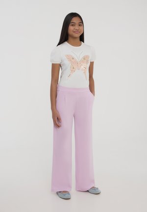 T-shirt bianco con maniche a sbuffo e un design di farfalla in paillettes rosa, abbinato a pantaloni larghi rosa chiaro e scarpe blu morbide.