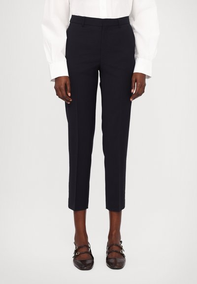 Pantalones navy a medida con corte ajustado, que presentan una textura suave y una longitud recortada. Combinados con zapatos oscuros y con tiras.