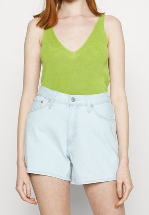 Groene geribbelde tanktop met een V-hals, gecombineerd met lichtblauwe denimshorts met een hoge taille en een sluiting met voorknop.