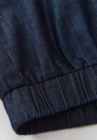 Tessuto denim scuro con una superficie liscia, caratterizzato da un orlo elasticizzato per un aspetto arricciato. Il colore è un blu navy profondo con una lucentezza sottile.