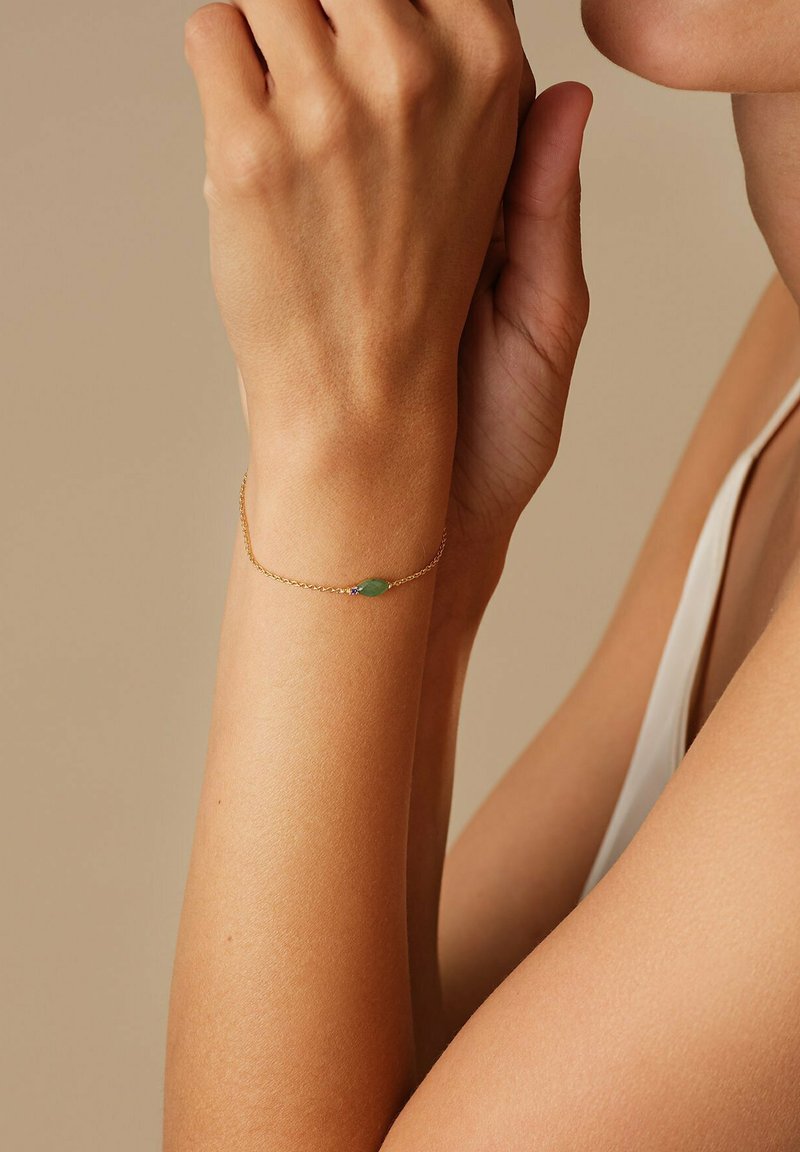 Guldkedjearmband med en grön stentopp. Armbandet har en känslig design och vilar på en handled med slät hud.