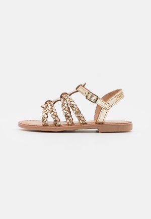 Sandali beige con cinturini intrecciati in colori metallici e neutri, con suola piatta e fibbia regolabile alla caviglia.