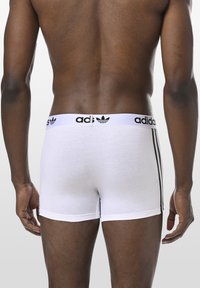 Weiße Baumwollboxershorts mit schwarzem Adidas-Logo-Gummibund und drei schwarzen Streifen an den Seiten. Glatte Textur, enganliegendes Design.