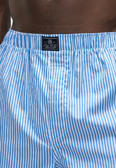 Κοντινό πλάνο της μέσης που φοράει σορτς με κάθετες μπλε και λευκές ρίγες με μαύρη ετικέτα Polo RL στο κέντρο της ελαστικής μέσης.