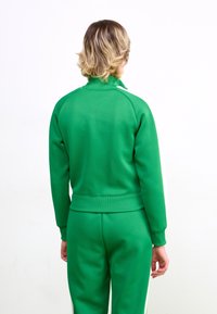 Sweatshirt vert et pantalon de survêtement assorti en tissu doux, avec un col haut et des poignets côtelés, des coutures visibles et une coupe décontractée.