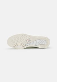 Semelle en caoutchouc blanc avec un motif de grip texturé comprenant des designs en zigzag et circulaires, et un petit logo sur le côté.