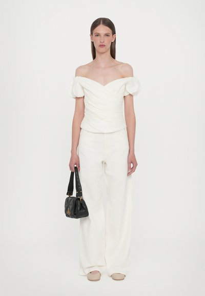White off-the-shoulder top with puff sleeves, textured fabric, paired with wide-leg white pants and a small black handbag.