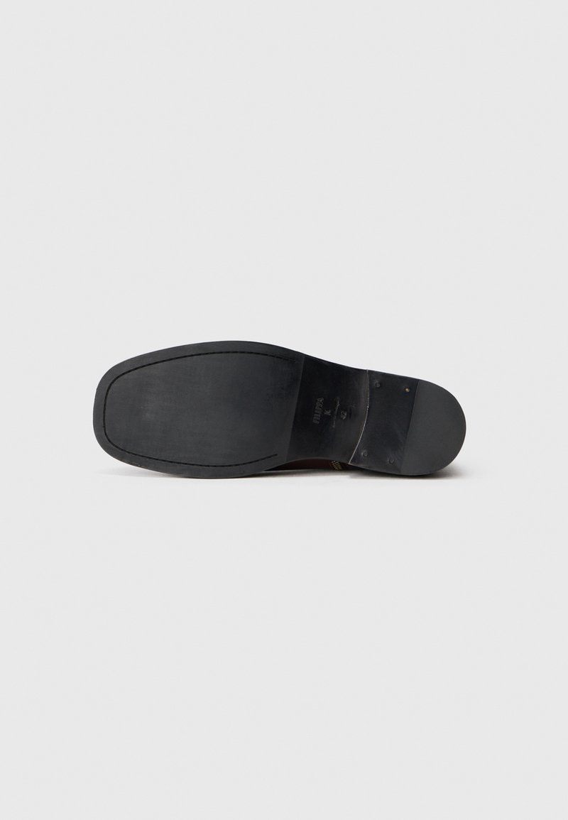 Semelle de chaussure noire avec une surface lisse, une forme arrondie et un motif de semelle minimal. Présente un talon visible et des accents en métal.
