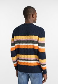 Maglione blu navy con texture a treccia, caratterizzato da righe orizzontali in arancione, giallo, rosa, grigio e bianco. Polsini e orlo a costine.