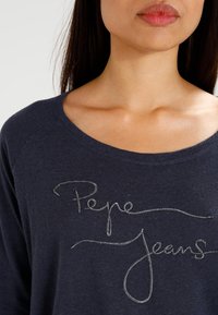 Rundhalsad skjorta i marinblått i mjukt tyg med silverbroderad text "Pepe Jeans" på framsidan.