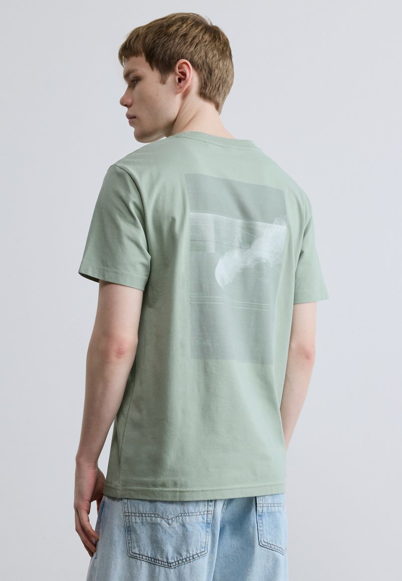 Light green short-sleeve t-shirt with a graphic print on the back, made of soft cotton. Features a relaxed fit and crew neckline.