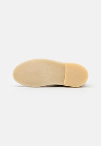 Sole di scarpa in suede color tan con texture liscia, forma arrotondata e tacco leggermente elevato per un comfort aggiunto. Design semplice e minimalista.