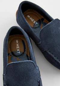 Scarpe slip-on in suede blu navy con una texture liscia, cuciture a contrasto e una soletta imbottita con un logo marrone.
