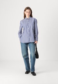 Blå og hvit stripet skjorte med krage, lange ermer, lomme på brystet, kombinert med lyseblå straight-leg jeans og svarte sko.