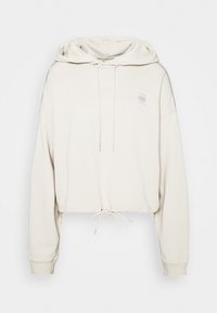 Ljust beige kort hoodie i mjukt tyg, med dragsko vid fållen, sid sömmar och en liten logga på bröstet.