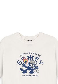 Crème-kleurige katoenen t-shirt met een marineblauw grafisch ontwerp van een cartoonfiguur die een fakkel en een tas met een dollar-teken vasthoudt, ronde teksten accenten.