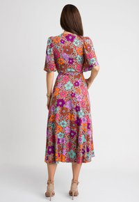 Długa, zwiewna sukienka z kolorowym kwiatowym nadrukiem w odcieniach różu, pomarańczy i turkusu na brązowym tle, z krótkimi rękawami i paskiem w talii.
