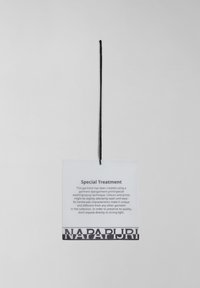 Étiquette de vêtement avec le texte "Traitement Spécial" détaillant les soins du vêtement ; attachée par un cordon noir et marquée "NAPAPIJRI" en bas.