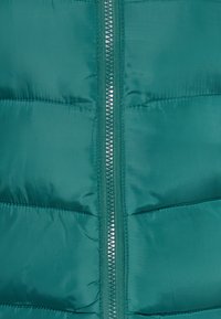Giacca imbottita color teal con zip frontale, presenta sezioni trapuntate e una texture liscia e lucida. La zip ha dettagli metallici.