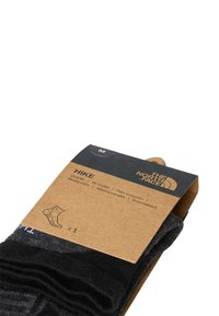 Czarne skarpetki trekkingowe z wyściełanym podbiciem, zapakowane z brązową tekturową etykietą zawierającą informacje o rozmiarze (M) oraz szczegóły produktu.