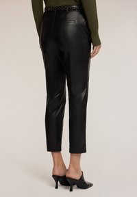 Czarne spodnie z ekoskóry o tapered fit, długości do kostek i kieszeniach. Połączone z czarnymi klapkami na obcasie i zielonym swetrem.