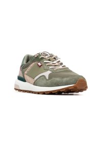 Zapatilla deportiva de ante verde y malla con suela blanca, detalles beige y cordones claros. Presenta paneles texturizados y una suela de goma para mayor tracción.