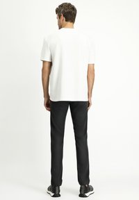 Maglietta bianca a maniche corte con collo rotondo, abbinata a pantaloni neri slim-fit e scarpe da ginnastica nere. Design semplice, senza motivi visibili.