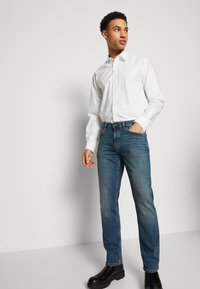 White button-up shirt, blue jeans, and black ankle boots. Shirt has a classic collar; jeans are mid-rise, straight-leg style.