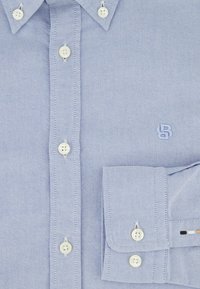 Chemise bleu clair à manches longues avec un tissu texturé, dotée de boutons blancs, d'une poche avec des coutures contrastées et d'un logo brodé.