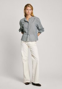 Camisa de cuadros verde y blanca con botones, de manga larga, con placket frontal y detalle de hombro fruncido, combinada con pantalones anchos color crema.