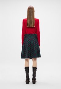 Κόκκινο μακρυμάνικο τοπ, πράσινη καρό φούστα με φαρδιά εφαρμογή και κόκκινες και μπλέ λεπτομέρειες, και μαύρες δερμάτινες μπότες μέχρι το γόνατο με κούμπωμα.