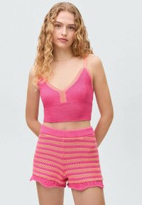 Ružový pletený crop top s výstrihom do V a zodpovedajúcimi šortkami s horizontálnymi pruhmi a scalloped okrajmi. Mäkká textura a priliehavý strih.