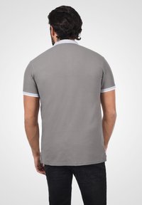 Polo gris à manches courtes avec un col et des accents de manches blancs. Texture douce avec une coupe droite et un détail subtil au dos.