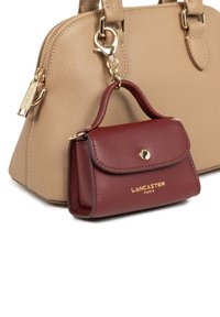 Borsa beige in pelle testurizzata con hardware dorato, accompagnata da una borsa in pelle bordeaux più piccola, impresso con "LANCASTER PARIS."