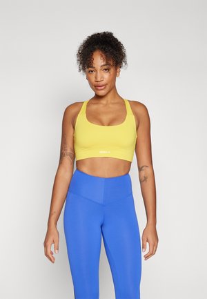 Yellow sports bra with thick straps; smooth texture and mid-length cut. Paired with high-waisted blue leggings, also with a smooth finish.