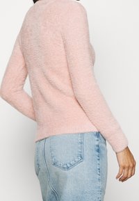 Maglione rosa fluffy con orlo a coste e scollatura rotonda, abbinato a jeans in denim azzurro chiaro, mostrando i dettagli della vista posteriore e laterale.